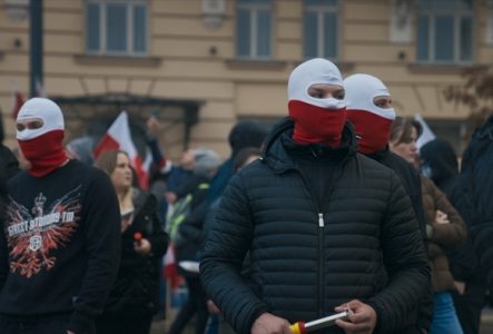 Manifestants masqués en blanc et rouge, couleurs du drapeau polonais, lors d'un rassemblement.