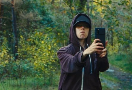 Une personne en sweat à capuche et casquette prenant un selfie en pleine forêt.