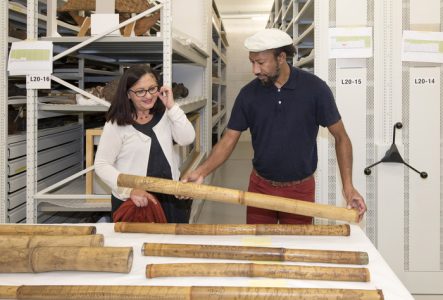 Sur cette image, Denis Pourawa, un poète et écrivain kanak (Nouvelle-Calédonie), est dans la réserve des collections du MEG avec la conservatrice des collections Océanie. Denis Pourawa a devant lui une série de bambou gravé kanak. Il en prend un dans les mains et pose son regard dessus. Les bambous kanak mesure environ 1m20 de long.